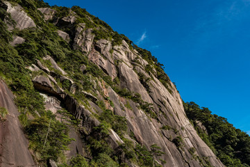 Fototapeta na wymiar rock face on the mountain top covered in green on a sunny day under blue sky