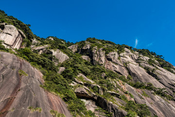 Fototapeta na wymiar rock face on the mountain top covered in green on a sunny day under blue sky