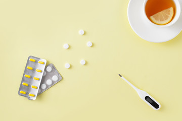 Pills, thermometer and cup of tea on yellow background. Cold and flu treatment set. Flat lay, top view. Free copy space.