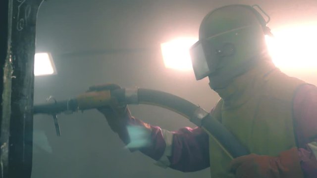 Man cleans metal surface by sandblaster gun in a metal construction factory. Shotblaster in a process