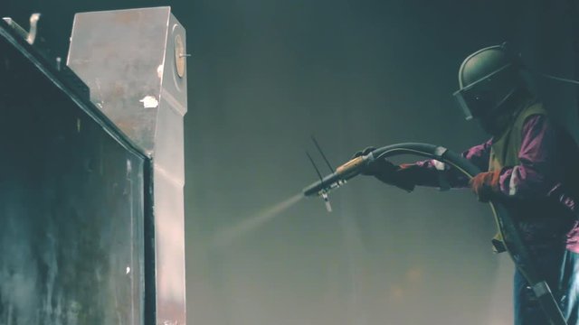 Man cleans metal surface by sandblaster gun in a metal construction factory. Shotblaster in a process