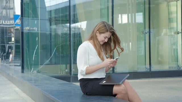 Young business woman talking is using smartphone in city park business center