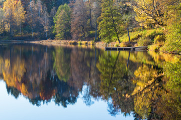 View of a lake with a jetty by the beach and reflections of autumn colors in the water