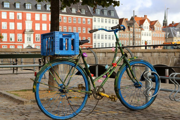 Bicycle in Denmark is a very popular means of transport. A blue, old bicycle parked in the parking lot. The background is a canal and the old part of the city of Copenhagen.