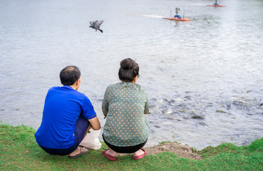 asian senior couple have activity together, feeding fish at the pond