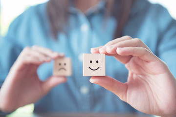 Close up customer hand choose smiley face and blurred sad face icon on wood cube, Service rating,...