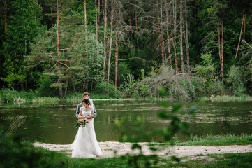 Portrait of an attractive groom and bride standing on nature in the park. Happy and joyful moment. Romantic couple of newlyweds near pond. Wedding ceremony near lake. Photography. Photo.