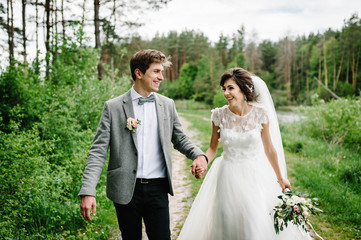 Romantic couple newlyweds, bride and groom is walking on a trail in an green park. Happy and joyful...