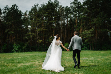 Attractive couple newlyweds is walking back on a trail in an green forest. Happy and joyful moment.