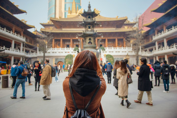 Rear view of young woman traveler taking photo picture at jing'an temple in china. Young asian...