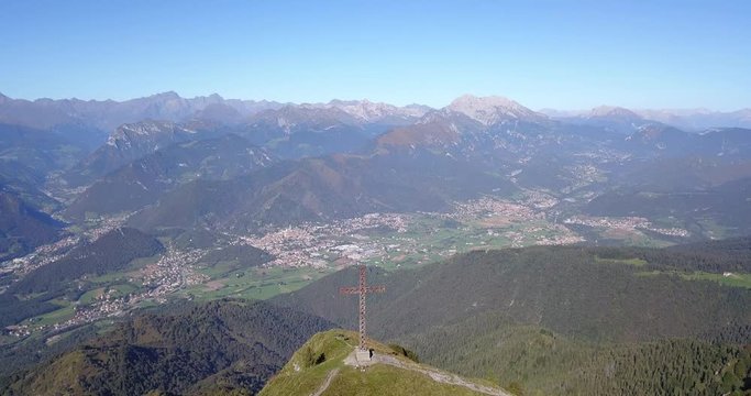 4K Drone aerial view to the Seriana valley and Orobie Alps in a clear and blue day. The cross at the top of the mountain. Landscape from Pizzo Formico Mountain, Bergamo, Italy