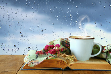 coffee cup on a rainy day over wooden table and window with rain drops background.