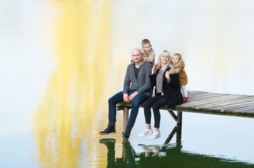 Happy family of four sit on the wooden pier in warm autumn day