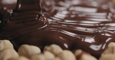 closeup covering roasted hazelnuts with melted dark chocolate