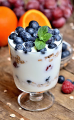 Yogurt with oatmeal, fresh blueberries and mint leaves and orange and grapes in background