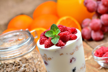 Yogurt, fresh raspberries in a glass and mint leaves, oranges, grapes and full glass of oatmeals in background - healthy breakfast concept