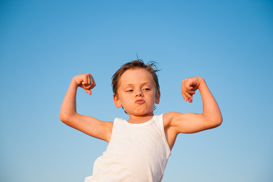 strong healthy little boy in shirt showing his muscles on blue sky background