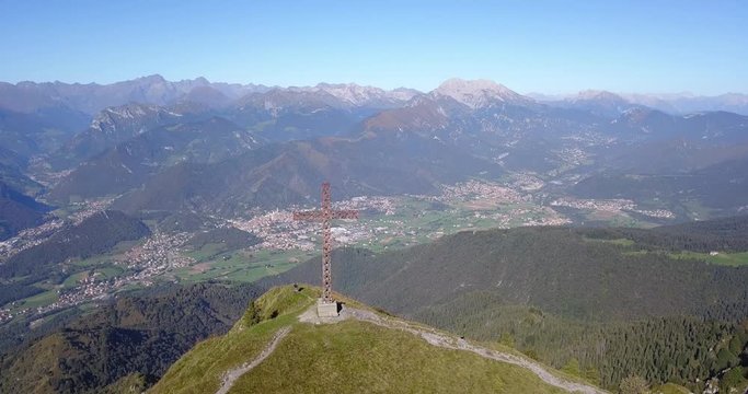4K Drone aerial view to the Seriana valley and Orobie Alps in a clear and blue day. The cross at the top of the mountain. Landscape from Pizzo Formico Mountain, Bergamo, Italy