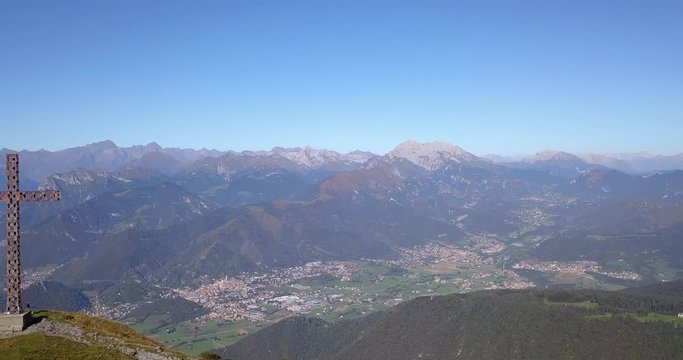 4K Drone aerial view to the Seriana valley and Orobie Alps in a clear and blue day. The cross at the top of the mountain. Landscape from Pizzo Formico Mountain, Bergamo, Italy
