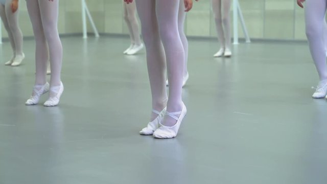 closeup legs of little ballerinas group in white shoes practicing in ballet studio. Young girls training positions of classical dance exercise. Childhood, dancing, lifestyle concept
