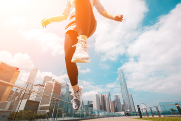 Woman runner jumping over the camera  with Hong Kong Cityscape in background - obrazy, fototapety, plakaty