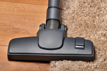 Close-up of head of vacuum cleaner on borderline of shaggy carpet and floating floor
