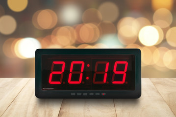 red led light illuminated numbers 2019 on digital electric alarm clock face on brown wooden table...