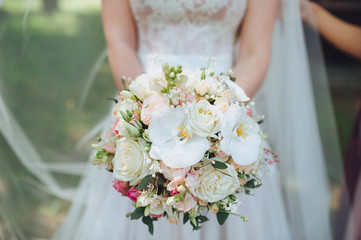 The bride in a white dress is holding a beautiful wedding bouquet in her hands. White orchids and...