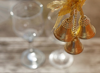 Closeup three golden Christmas bells hanging on the blurred background of two wineglasses