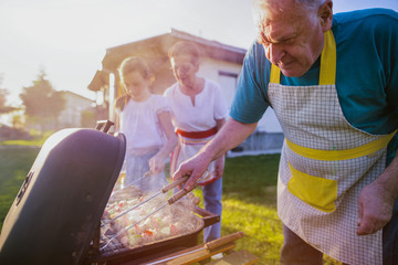 Older cheerful couple making barbeque in backyard. Spending some time with their family.