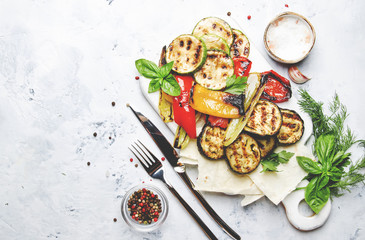 Grilled colorful vegetables, aubergines, zucchini, pepper with spice and green basil on serving board on white background, top view