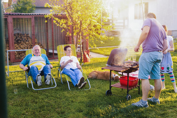 Picture of older couple lying down in chairs in their backyard and enjoining after good barbeque