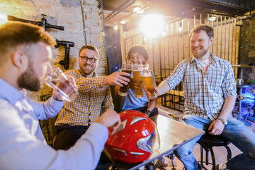 Male happy friends sitting in a bar and drinking beer. One man is drinking water while other are...