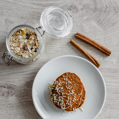 Still life morning breakfast of pancakes with honey and sprinkled with sesame seeds, cinnamon sticks and muesli in glass on a white plate on a wooden background.