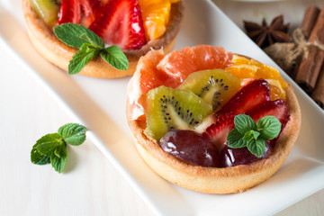 Fresh fruit and berry tart dessert with toss sugar on wooden background. Delicious sweet cake with raspberries, grapes, strawberries, cherry, kiwi, grapefruit and cream.