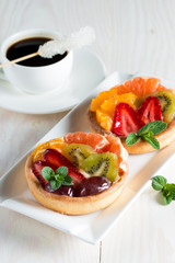 Fresh fruit and berry tart dessert with toss sugar on wooden background. Delicious sweet cake with raspberries, grapes, strawberries, cherry, kiwi, grapefruit and cream.