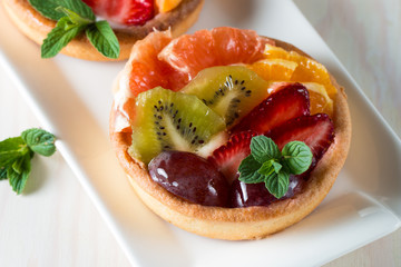Fresh fruit and berry tart dessert with toss sugar on wooden background. Delicious sweet cake with raspberries, grapes, strawberries, cherry, kiwi, grapefruit and cream.