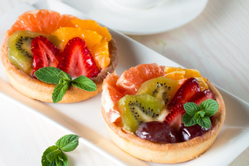 Fresh fruit and berry tart dessert with toss sugar on wooden background. Delicious sweet cake with raspberries, grapes, strawberries, cherry, kiwi, grapefruit and cream.