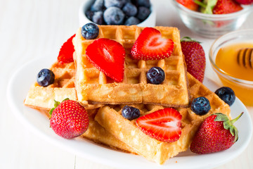 Photo of fresh homemade food made of berry Belgian waffles with honey, chocolate, strawberry, blueberry, maple syrup and cream. Healthy dessert breakfast concept with juice. 