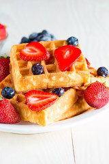 Photo of fresh homemade food made of berry Belgian waffles with honey, chocolate, strawberry, blueberry, maple syrup and cream. Healthy dessert breakfast concept with juice. 