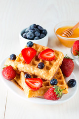 Photo of fresh homemade food made of berry Belgian waffles with honey, chocolate, strawberry, blueberry, maple syrup and cream. Healthy dessert breakfast concept with juice. 