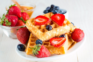 Photo of fresh homemade food made of berry Belgian waffles with honey, chocolate, strawberry, blueberry, maple syrup and cream. Healthy dessert breakfast concept with juice. 