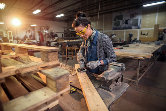Middle aged professional female carpenter working with sandpaper in her workshop.