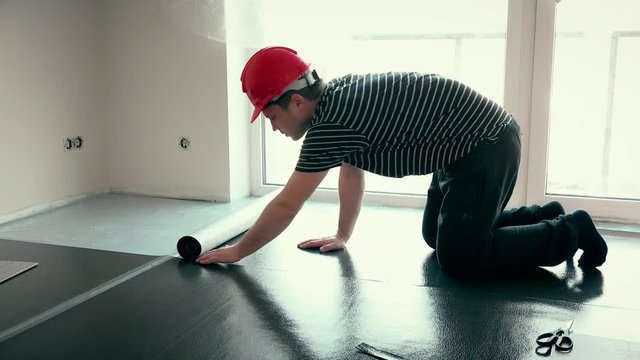 professional builder man with red helmet lay underlay mat deck in new room