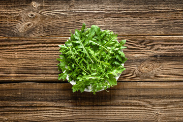 Fresh arugula leaves on plate on wooden background