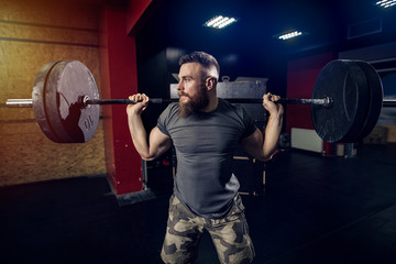 Naklejka na ściany i meble Bearded strong sporty man lifting heavy weight in dark room.