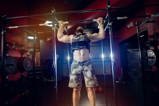 Strong focused bearded man holding on bar in gym.