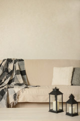 Autumn (winter) concept - coziness and warmth in the house. Beige sofa with plaid and pillows in the living room.