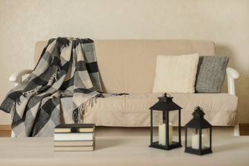 Autumn (winter) concept - coziness and warmth in the house. Beige sofa with plaid and pillows in the living room.