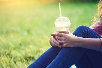 young girl sitting in the park with cocktail on plastic cup with a straw in her hands